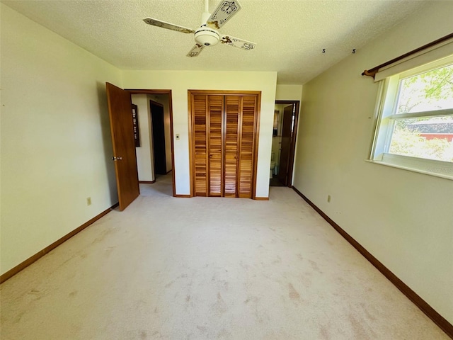 unfurnished bedroom featuring a ceiling fan, a textured ceiling, a closet, baseboards, and light colored carpet