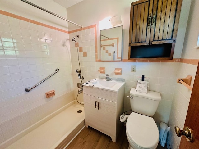 bathroom with toilet, vanity, tiled shower, wood finished floors, and tile walls