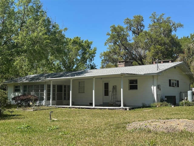 rear view of house featuring central AC unit, a lawn, and a sunroom