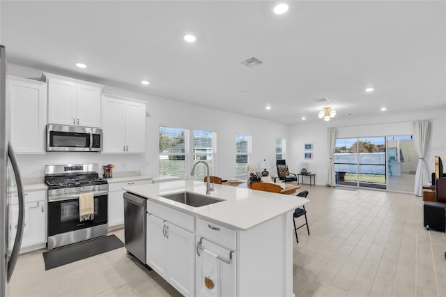 kitchen with an island with sink, a sink, stainless steel appliances, light countertops, and open floor plan