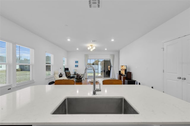 kitchen featuring visible vents, a sink, light stone counters, open floor plan, and recessed lighting