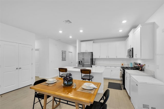 kitchen with visible vents, a kitchen island with sink, a sink, appliances with stainless steel finishes, and light countertops