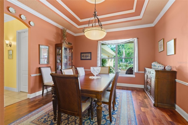 dining area with a tray ceiling, wood finished floors, arched walkways, and ornamental molding