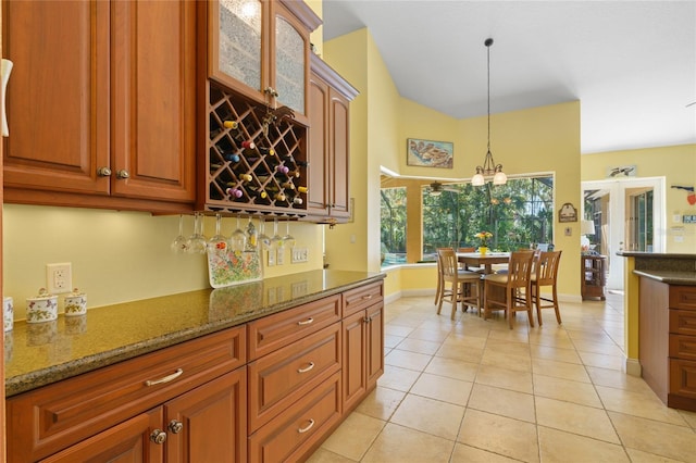 kitchen featuring dark stone countertops, brown cabinetry, light tile patterned flooring, glass insert cabinets, and decorative light fixtures