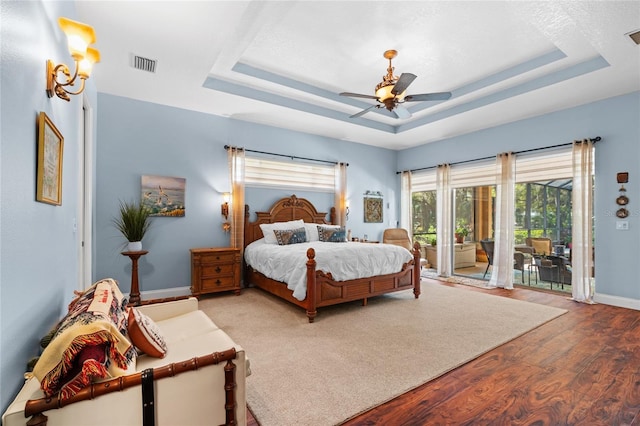 bedroom with visible vents, a raised ceiling, wood finished floors, and access to outside