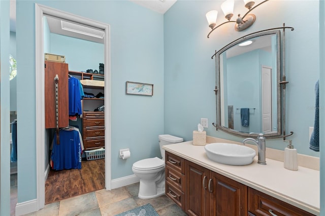 bathroom with vanity, baseboards, a notable chandelier, a walk in closet, and toilet