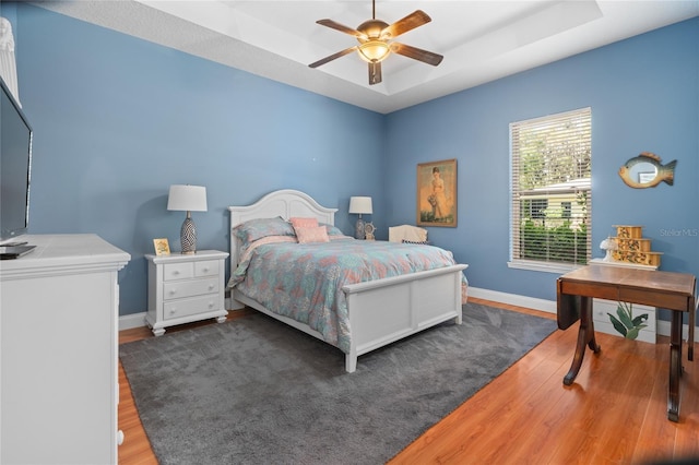 bedroom featuring ceiling fan, a tray ceiling, baseboards, and wood finished floors