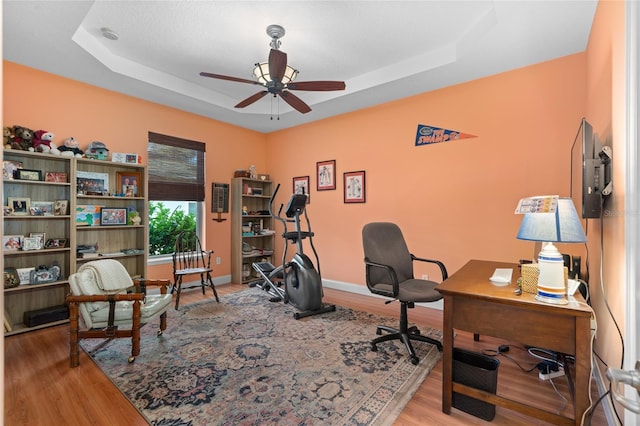 home office with a raised ceiling, wood finished floors, a ceiling fan, and baseboards