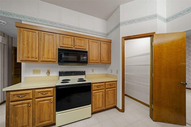 kitchen with light countertops, brown cabinetry, black microwave, and range with electric stovetop