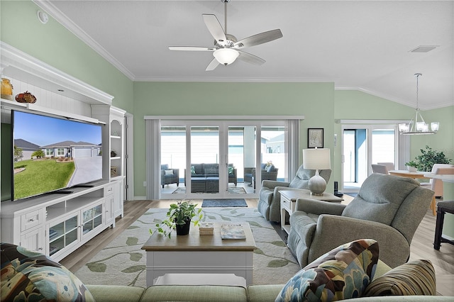 living room featuring vaulted ceiling, ceiling fan with notable chandelier, light wood-type flooring, and ornamental molding