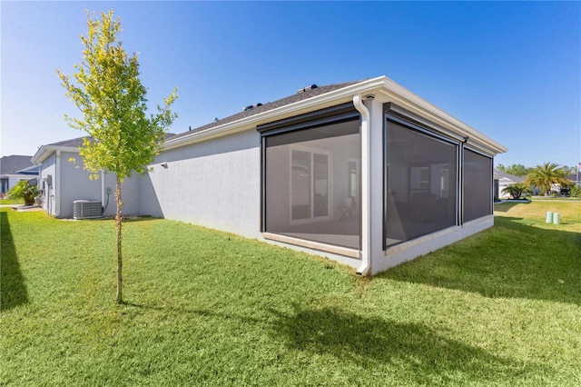 back of house with central air condition unit, a lawn, stucco siding, and a sunroom