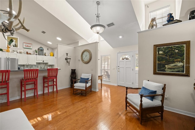 living area with visible vents, baseboards, light wood-style floors, and high vaulted ceiling