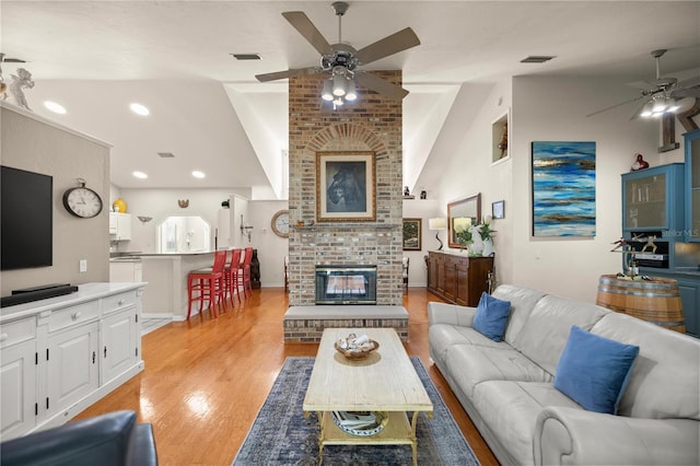 living room featuring visible vents, light wood-style flooring, a brick fireplace, and ceiling fan