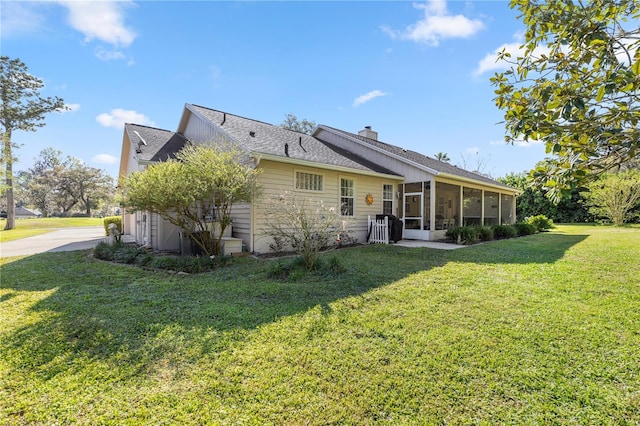 back of property with a chimney, a yard, and a sunroom