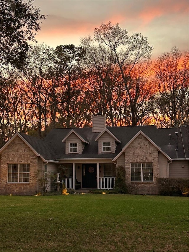 new england style home featuring a porch, a chimney, and a front yard