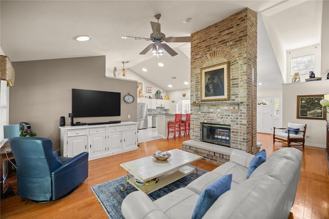 living area with high vaulted ceiling, light wood-style floors, a ceiling fan, and a brick fireplace