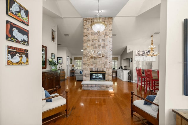 living area with an inviting chandelier, a brick fireplace, visible vents, high vaulted ceiling, and wood finished floors