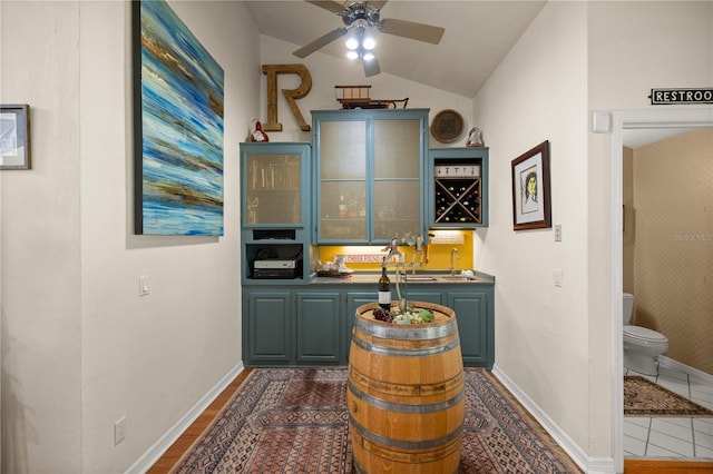 bar featuring indoor wet bar, baseboards, lofted ceiling, a sink, and ceiling fan