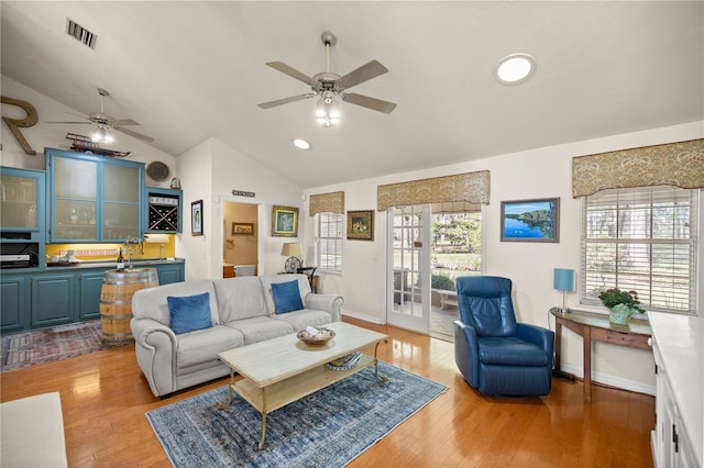 living room with light wood-type flooring, vaulted ceiling, a ceiling fan, and visible vents