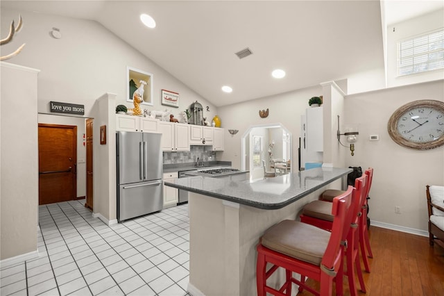 kitchen with visible vents, appliances with stainless steel finishes, white cabinetry, decorative backsplash, and a breakfast bar area