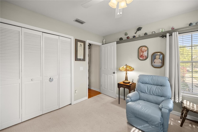 living area featuring light carpet, visible vents, baseboards, and ceiling fan