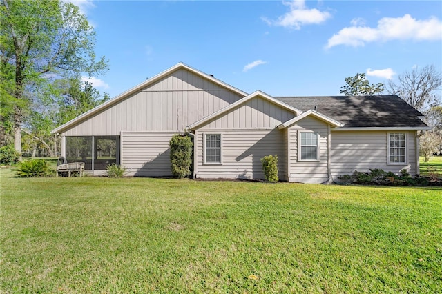 rear view of house with a sunroom, roof with shingles, and a yard