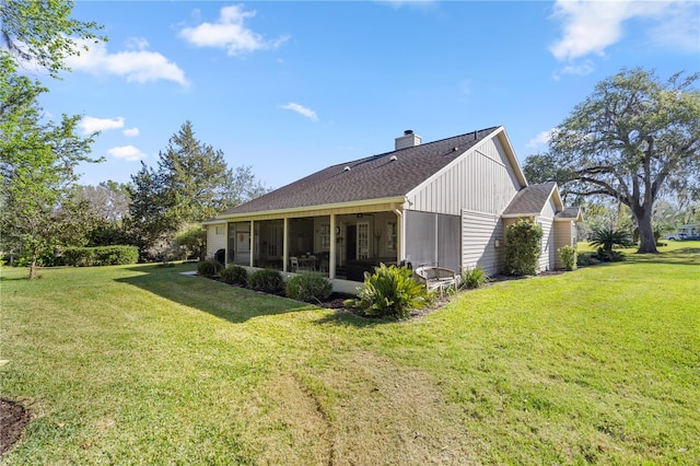 back of property featuring roof with shingles, a sunroom, a lawn, and a chimney