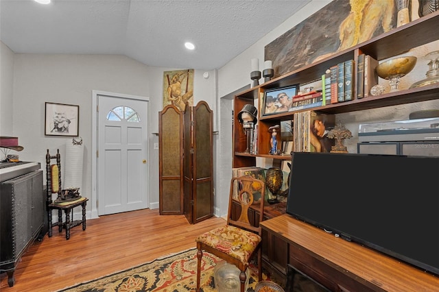 foyer featuring baseboards, a textured ceiling, lofted ceiling, and light wood-style floors