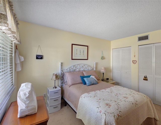 carpeted bedroom featuring visible vents, two closets, and a textured ceiling