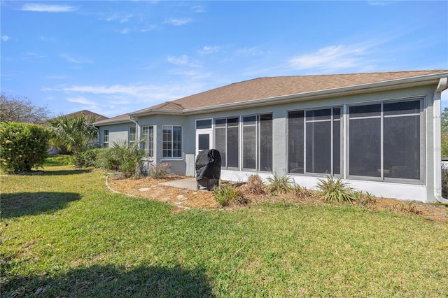 rear view of house with stucco siding, a yard, and a sunroom