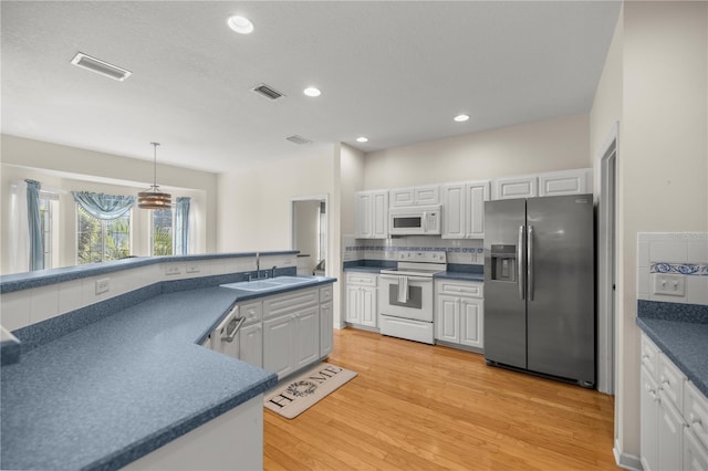 kitchen with dark countertops, visible vents, white appliances, and a sink