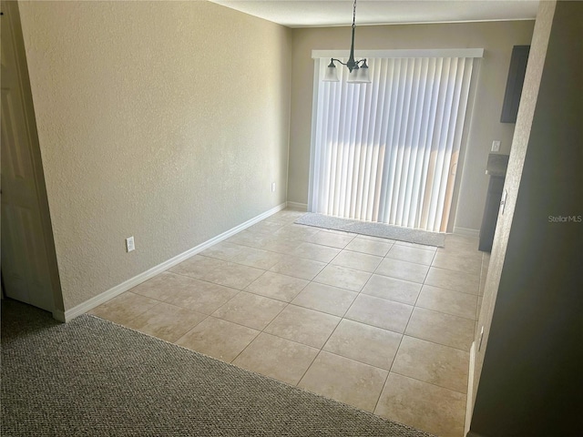 empty room featuring an inviting chandelier, light tile patterned floors, a textured wall, and baseboards