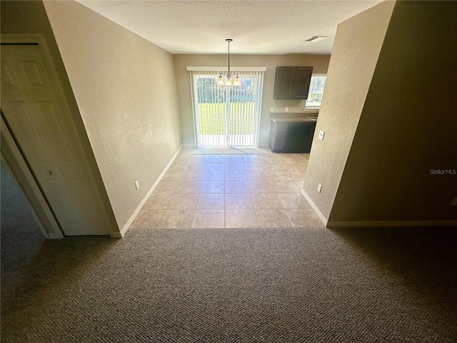 unfurnished dining area featuring visible vents, light carpet, a notable chandelier, baseboards, and a textured wall