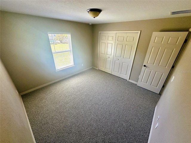 unfurnished bedroom with visible vents, a textured ceiling, a closet, carpet flooring, and baseboards