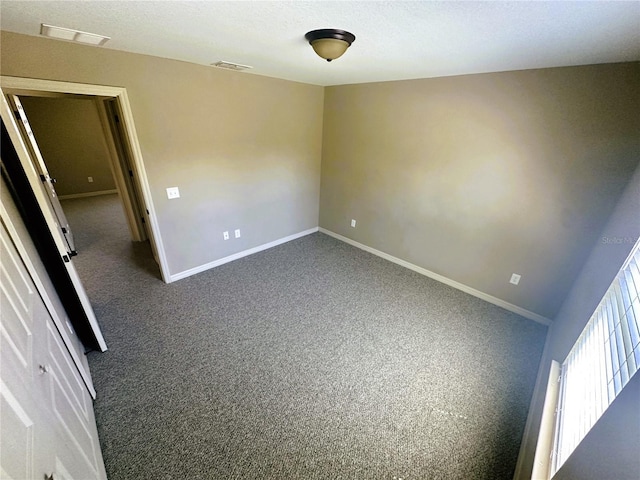 spare room with baseboards, visible vents, dark carpet, and a textured ceiling