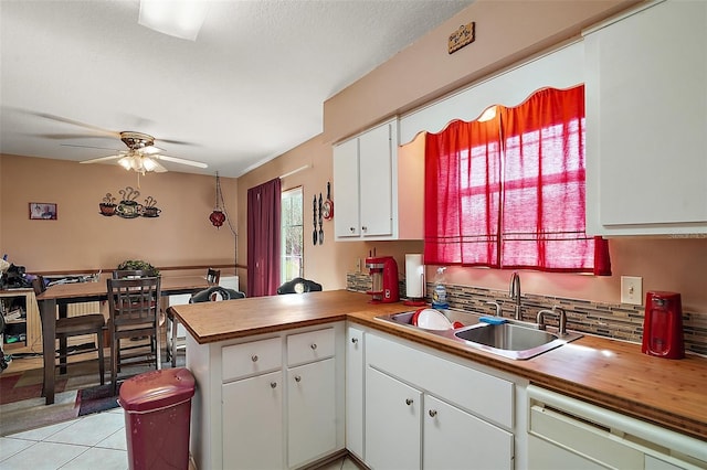 kitchen featuring a sink, white cabinetry, a peninsula, white dishwasher, and light tile patterned floors