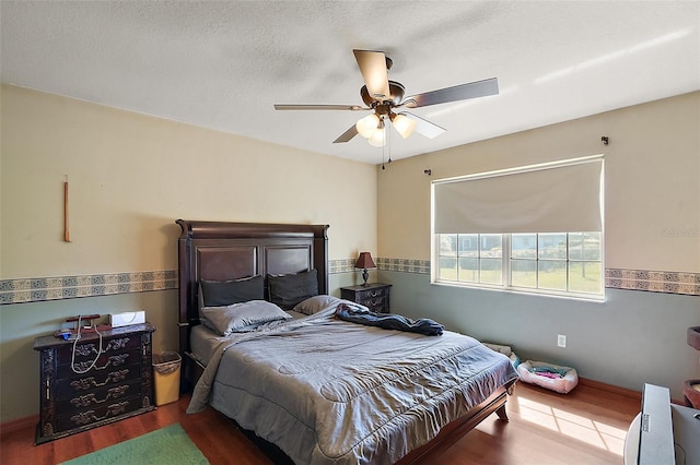 bedroom with a ceiling fan, wood finished floors, baseboards, and a textured ceiling