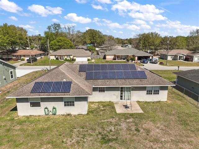 rear view of property featuring solar panels, a patio, a lawn, and roof with shingles