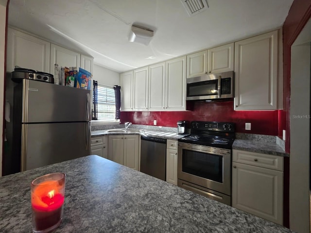 kitchen with a sink, stainless steel appliances, dark countertops, and visible vents