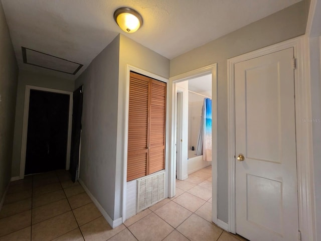 hall with light tile patterned floors, visible vents, baseboards, and attic access