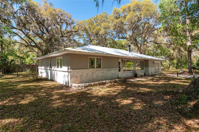 view of side of property featuring brick siding, a lawn, metal roof, and fence