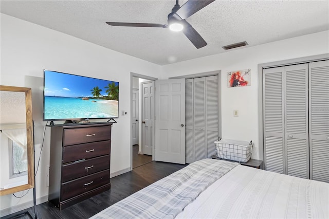 bedroom with visible vents, ceiling fan, multiple closets, dark wood-style floors, and a textured ceiling