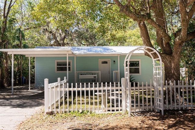 view of front of house featuring concrete driveway, a porch, a fenced front yard, and metal roof