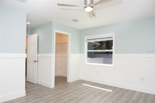 empty room featuring visible vents, light wood-style floors, a ceiling fan, and a wainscoted wall