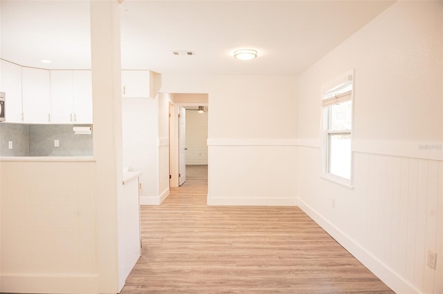 hall with visible vents, a wainscoted wall, and light wood finished floors