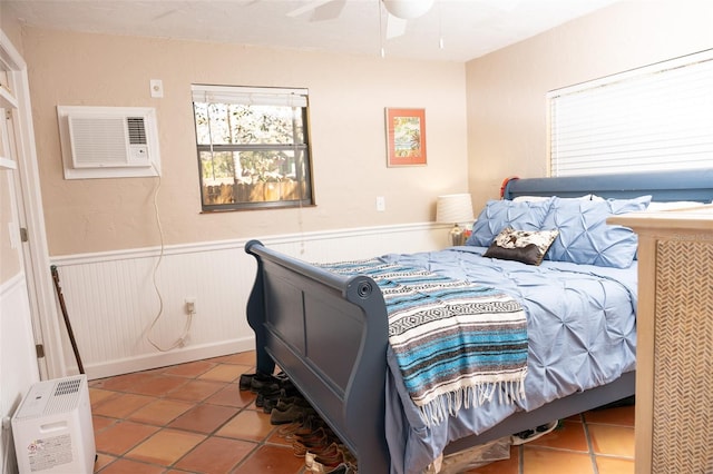 bedroom with tile patterned floors, wainscoting, a ceiling fan, and a wall unit AC