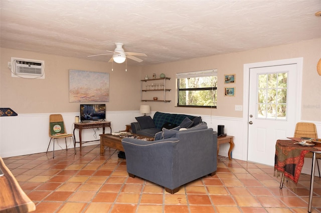 tiled living room with ceiling fan, a textured ceiling, a wall mounted AC, and wainscoting