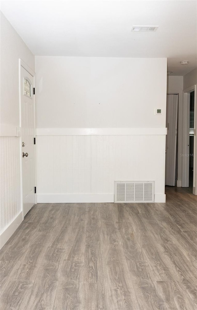 unfurnished room with visible vents, wood finished floors, and wainscoting