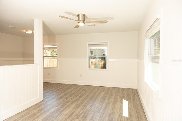 unfurnished room with a wainscoted wall, visible vents, a ceiling fan, and wood finished floors