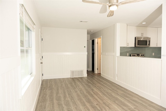 unfurnished living room featuring visible vents, light wood-style floors, wainscoting, and a ceiling fan